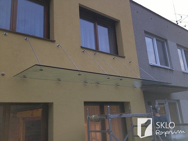 Dlouhá skleněná stříška nad vchody do domu
